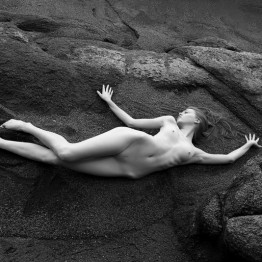 naked blond girl lying on a rock
